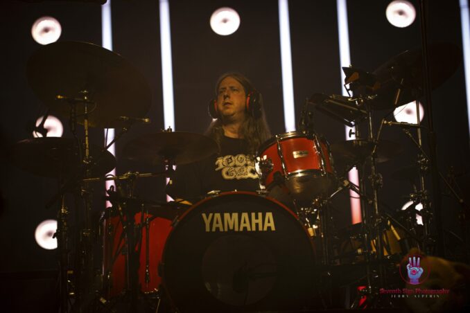 A drummer sits behind the drum kit.