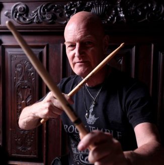 Portrait photo of Chris Slade holding drum sticks